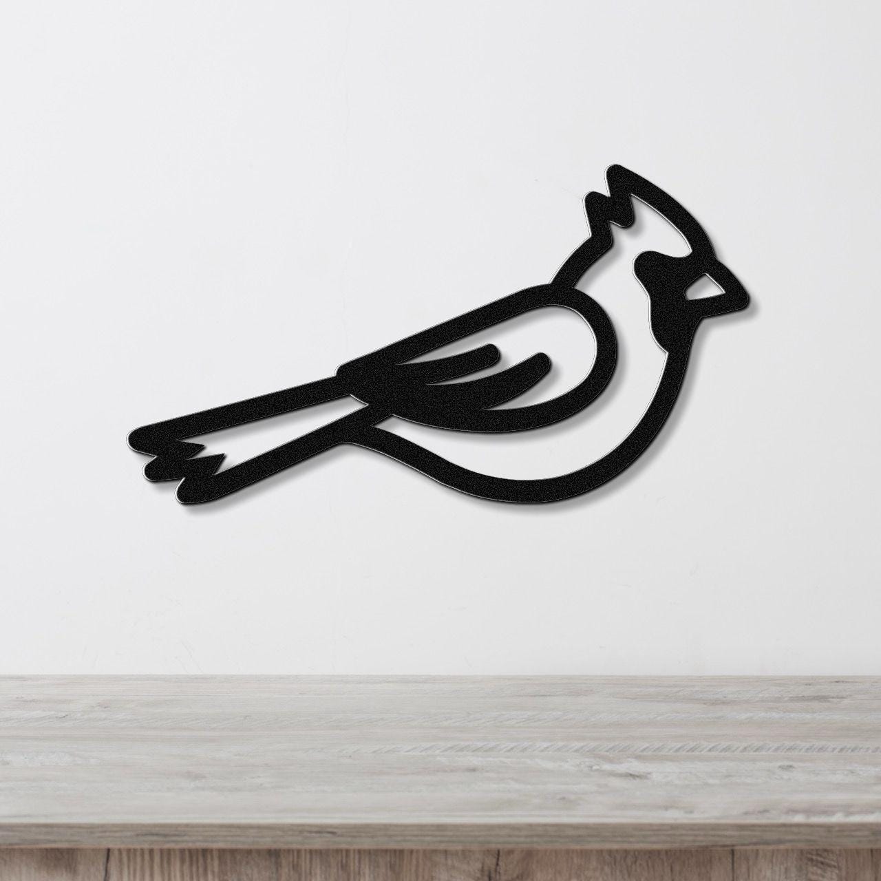 Black metal cardinal wall art with a minimalist silhouette design, mounted on a white wall above a light wood surface.
