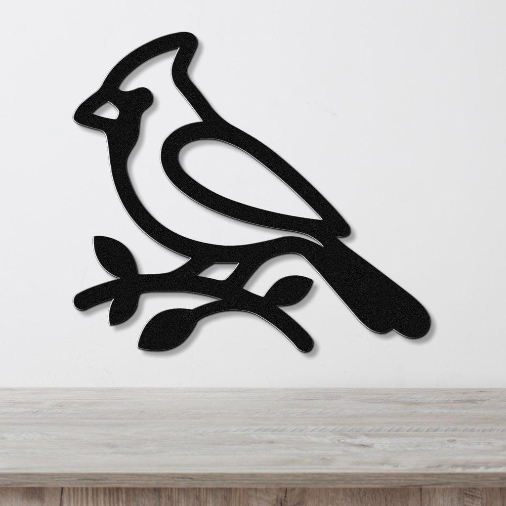 Black metal cardinal wall art silhouette perched on a branch, mounted on a white wall above a light wood counter.