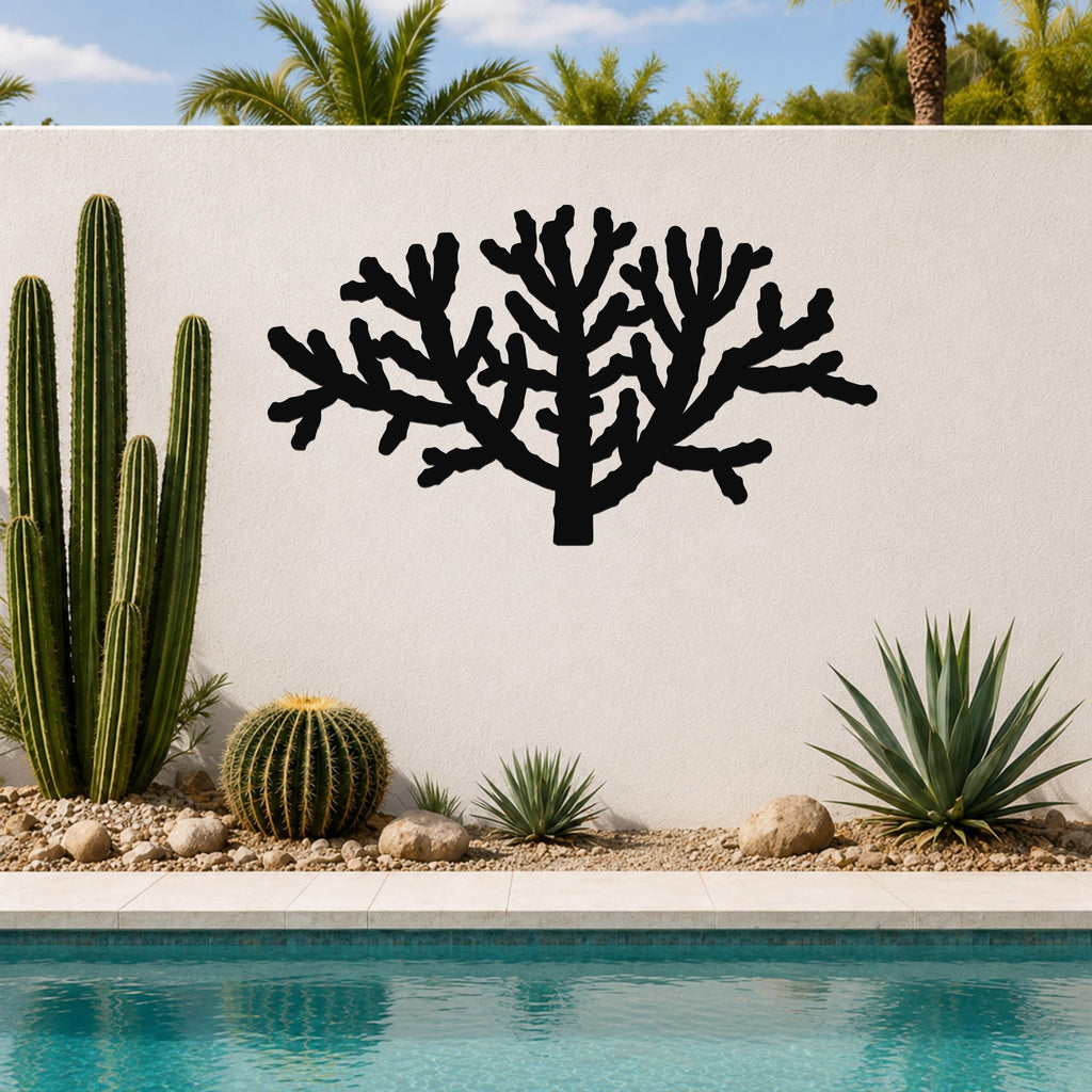 Black metal Cholla cactus wall art with branching silhouette, mounted on a white outdoor wall above a poolside garden.