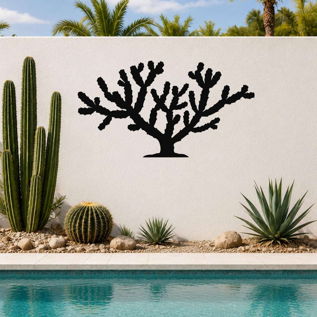Black metal Cholla cactus wall art with branching silhouette, mounted on a white outdoor wall beside a pool and desert plants.