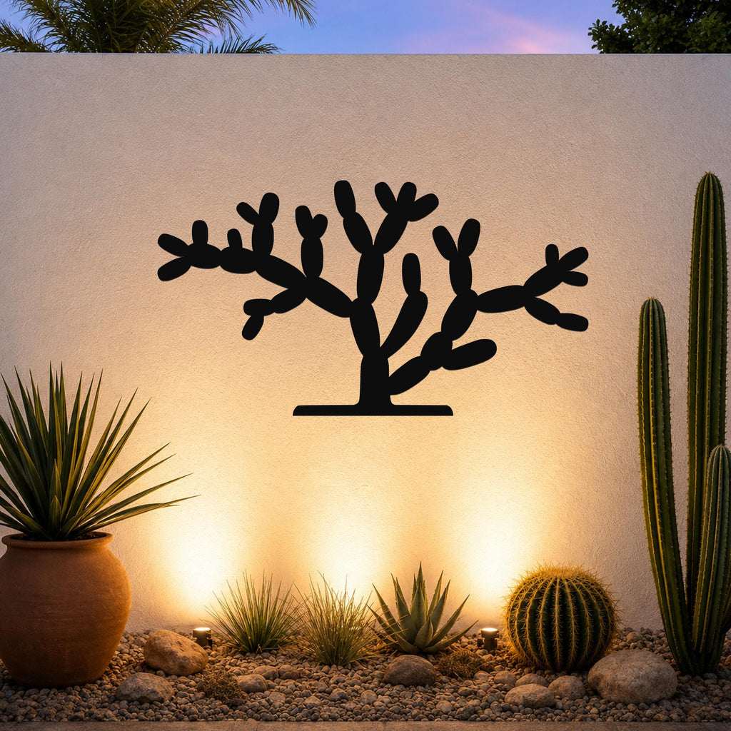 Black metal Cholla cactus wall art with branching cutouts, mounted on a textured outdoor wall above a desert garden with potted plants and ground lights.