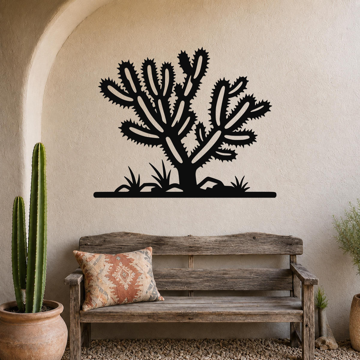 Black metal Cholla cactus wall art with spiky branch cutouts, mounted on a beige stucco wall above a wooden bench in a southwestern-style patio.