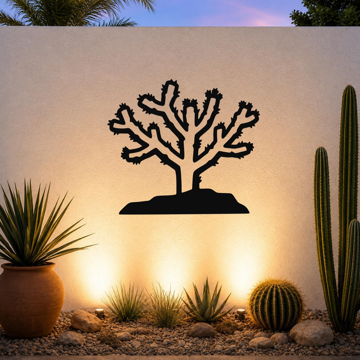 Black metal Cholla cactus wall art silhouette with branching arms and spines, mounted on a textured outdoor wall above a desert garden with potted succulents and ground lights.