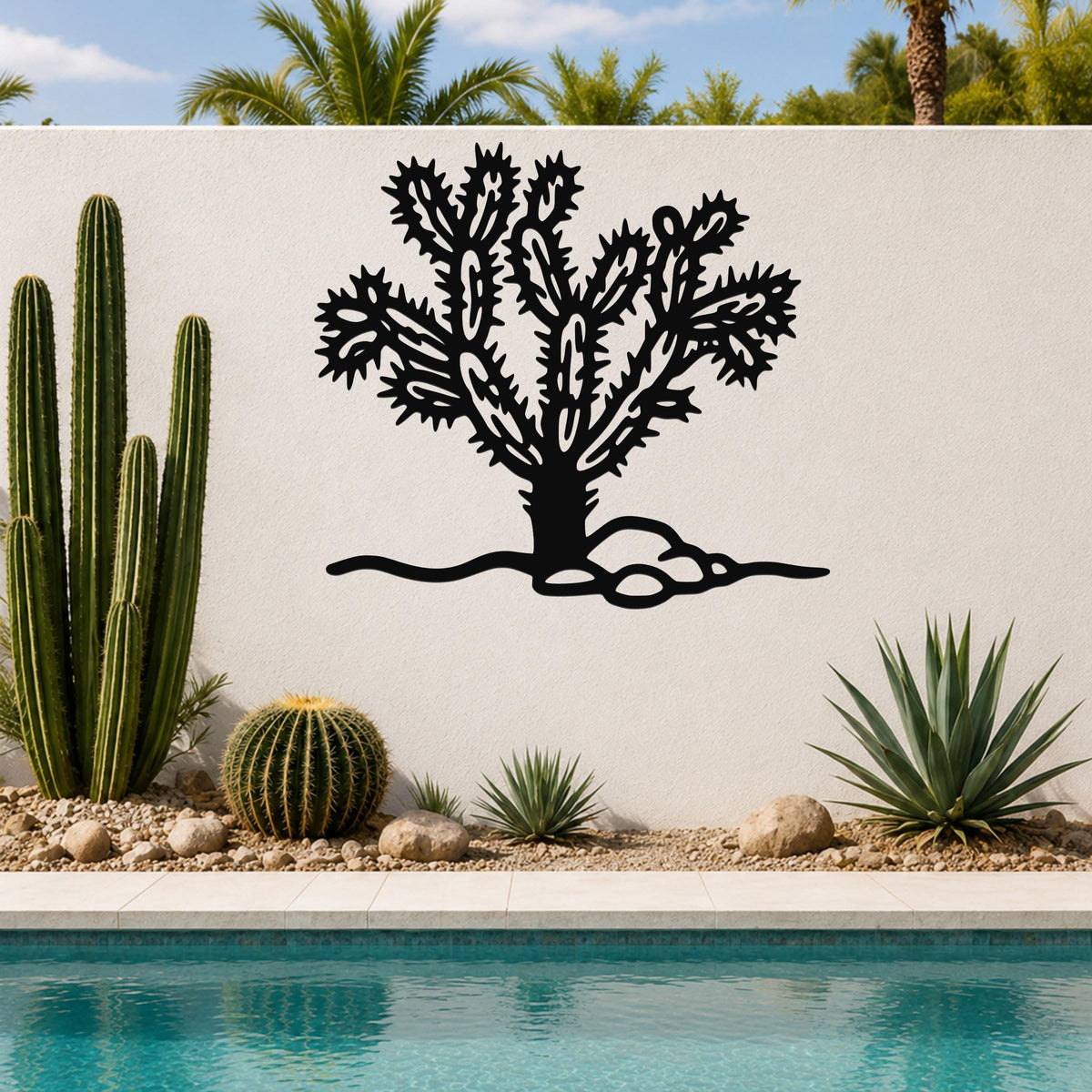 Black metal Cholla cactus wall art with intricate branch cutouts, mounted on a white outdoor wall above a poolside garden.