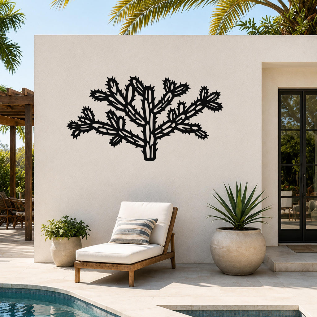 Black metal Cholla cactus wall art with intricate branch and spine cutouts, mounted on a white outdoor wall above a lounge chair near a pool.