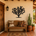 Black metal Cholla cactus wall art silhouette mounted on a stucco wall above a wooden bench in a rustic patio entryway.