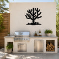 Black metal Cholla cactus wall art silhouette mounted on a beige outdoor wall above a built-in grill and counter.