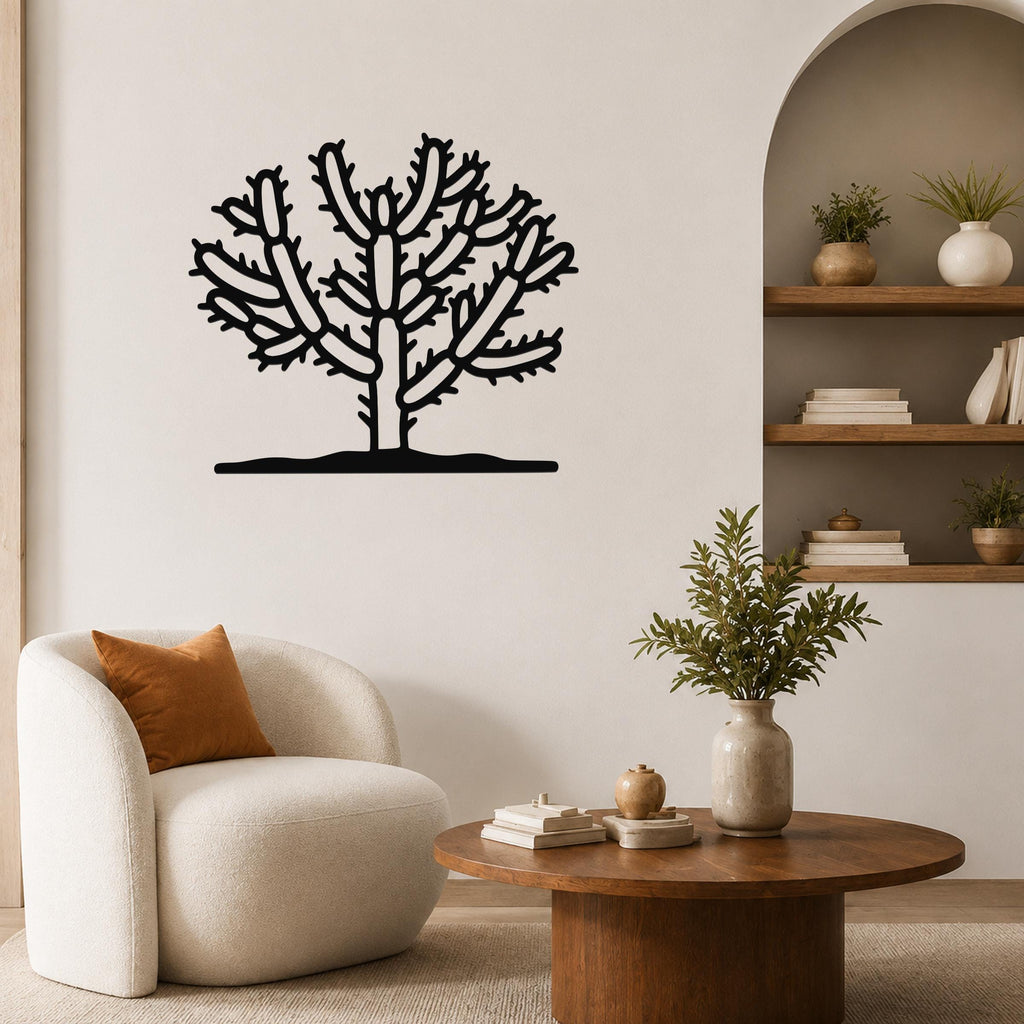 Black metal Cholla cactus wall art with branching silhouette, mounted on a living room wall above a white armchair.