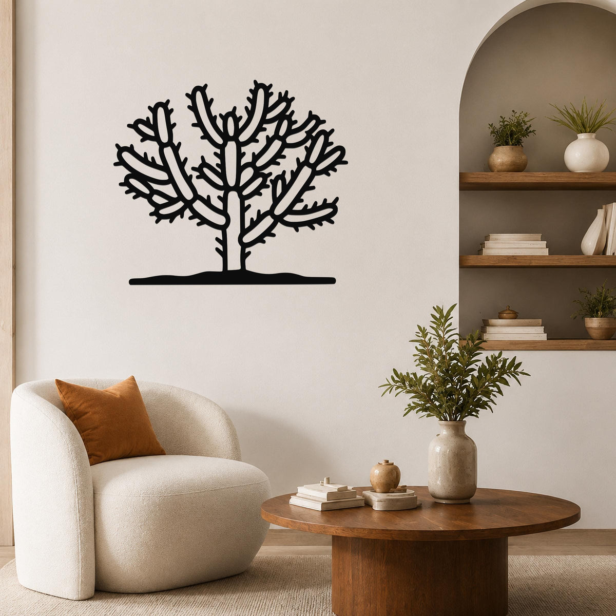 Black metal Cholla cactus wall art with branching silhouette, mounted on a living room wall above a white armchair.