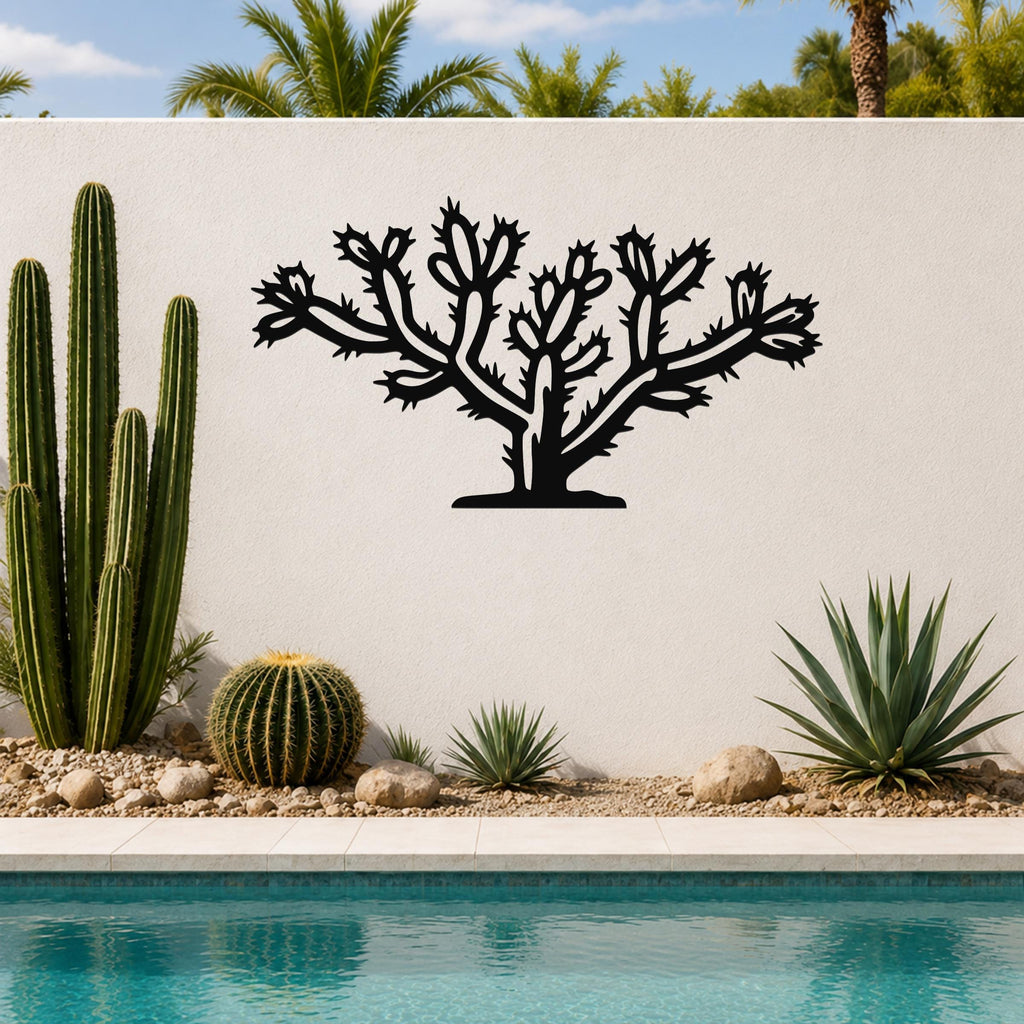 Black metal Cholla cactus wall art with detailed branch and spine cutouts, mounted on a white outdoor wall above a poolside garden.