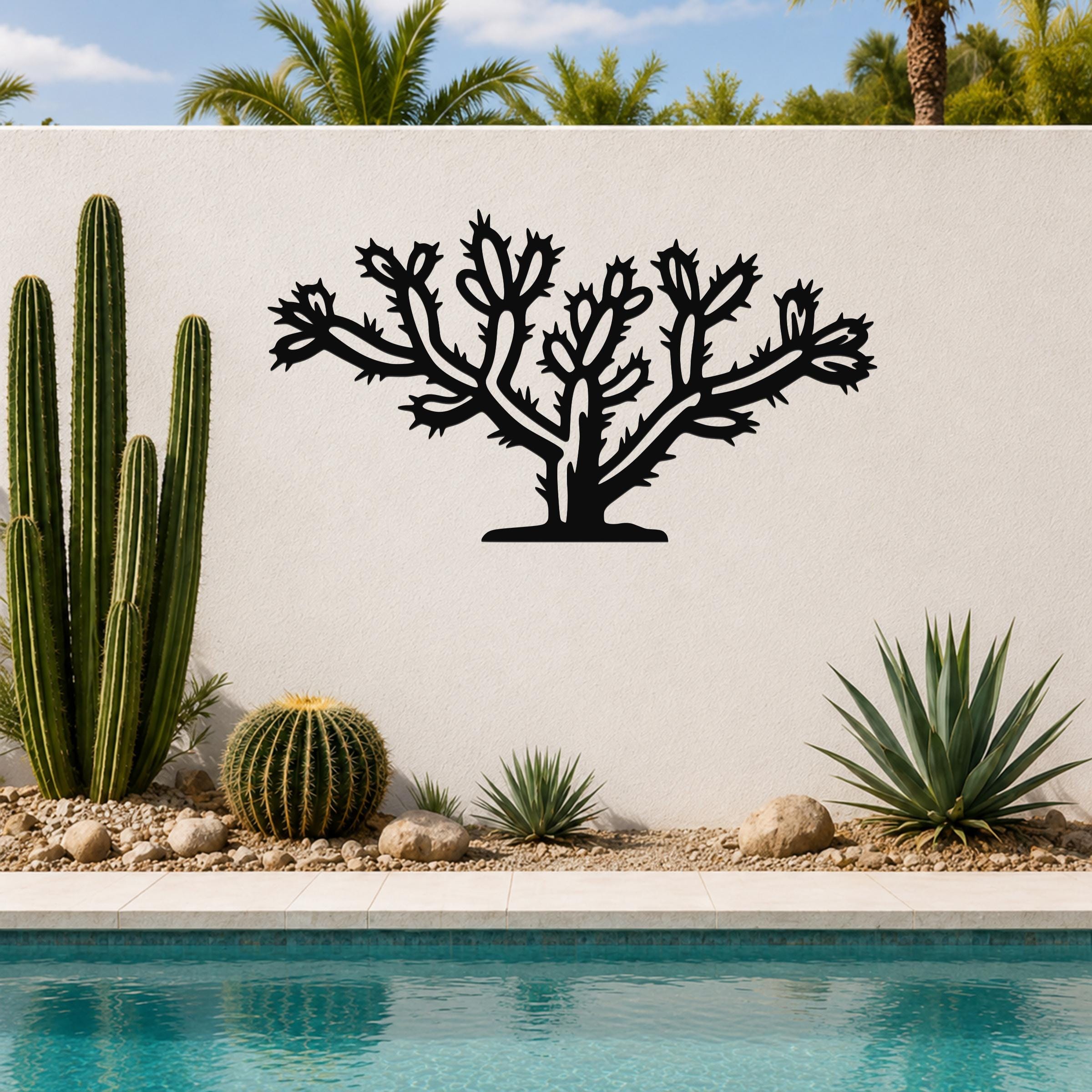 Black metal Cholla cactus wall art with detailed branch and spine cutouts, mounted on a white outdoor wall above a poolside garden.