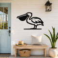 Black metal pelican wall art with a silhouette cutout, mounted on a white shiplap wall above a wooden bench in a coastal entryway.