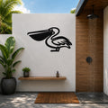 Black metal pelican wall art silhouette mounted on a white outdoor wall above a wooden shelf in a tropical shower area.