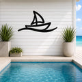 Black metal wall art in a sailboat silhouette with wave motion lines, mounted on a white shiplap wall above a pool in a coastal outdoor space.