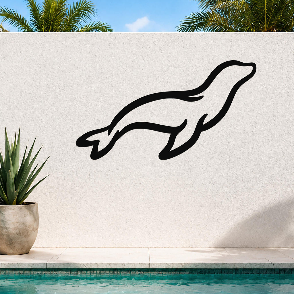 Black metal sea lion wall art with a sleek silhouette design, mounted on an outdoor white wall above a pool with palm trees in the background.