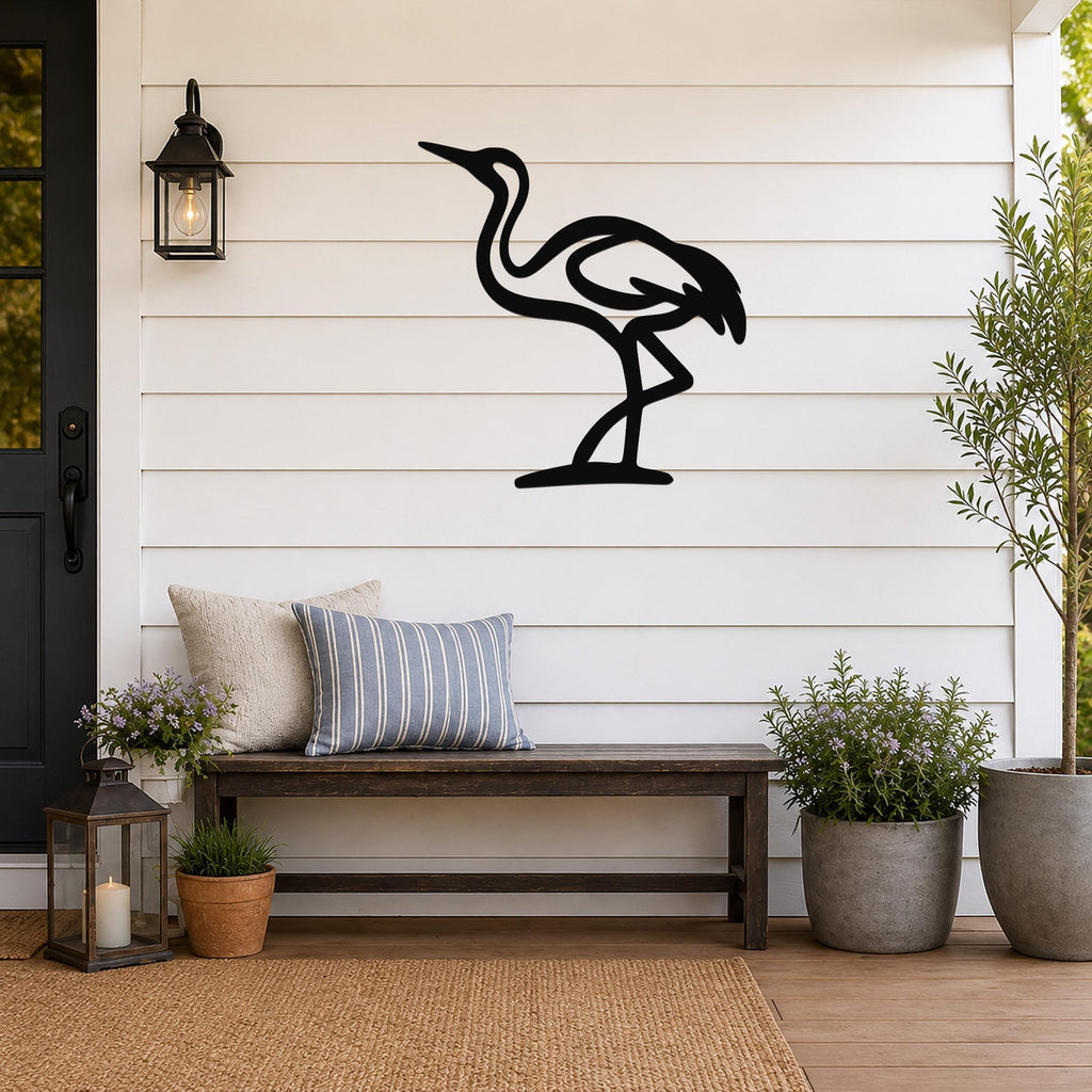 Black metal crane wall art in a minimalist silhouette style, mounted on a white shiplap wall above a wooden bench on a porch.