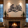 Black metal wall art silhouette of a cyclist on a trail with pine trees, mounted above a stone fireplace in a living room.