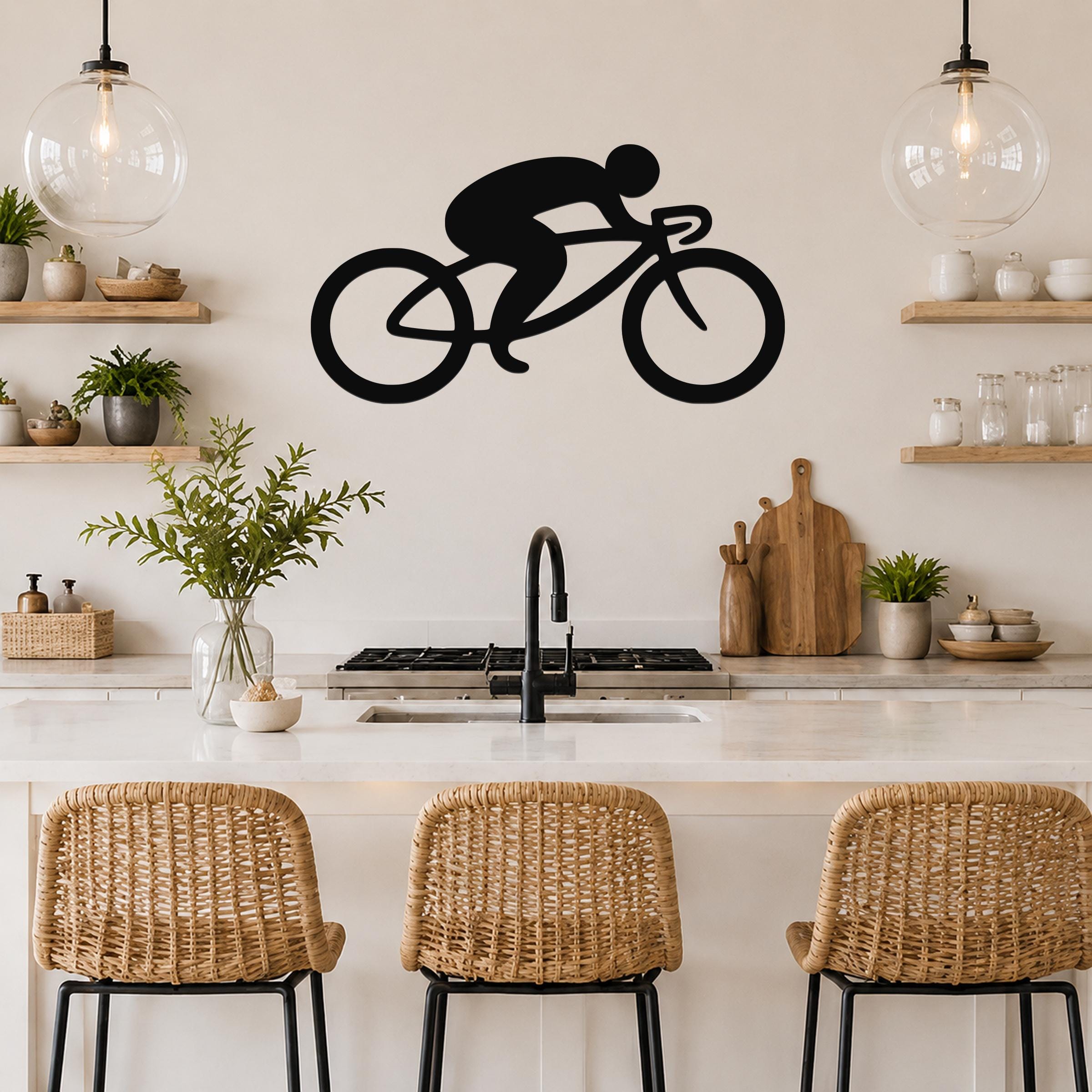 Black metal cycling wall art silhouette of a rider on a bike, mounted above a kitchen counter with open shelves and pendant lights.