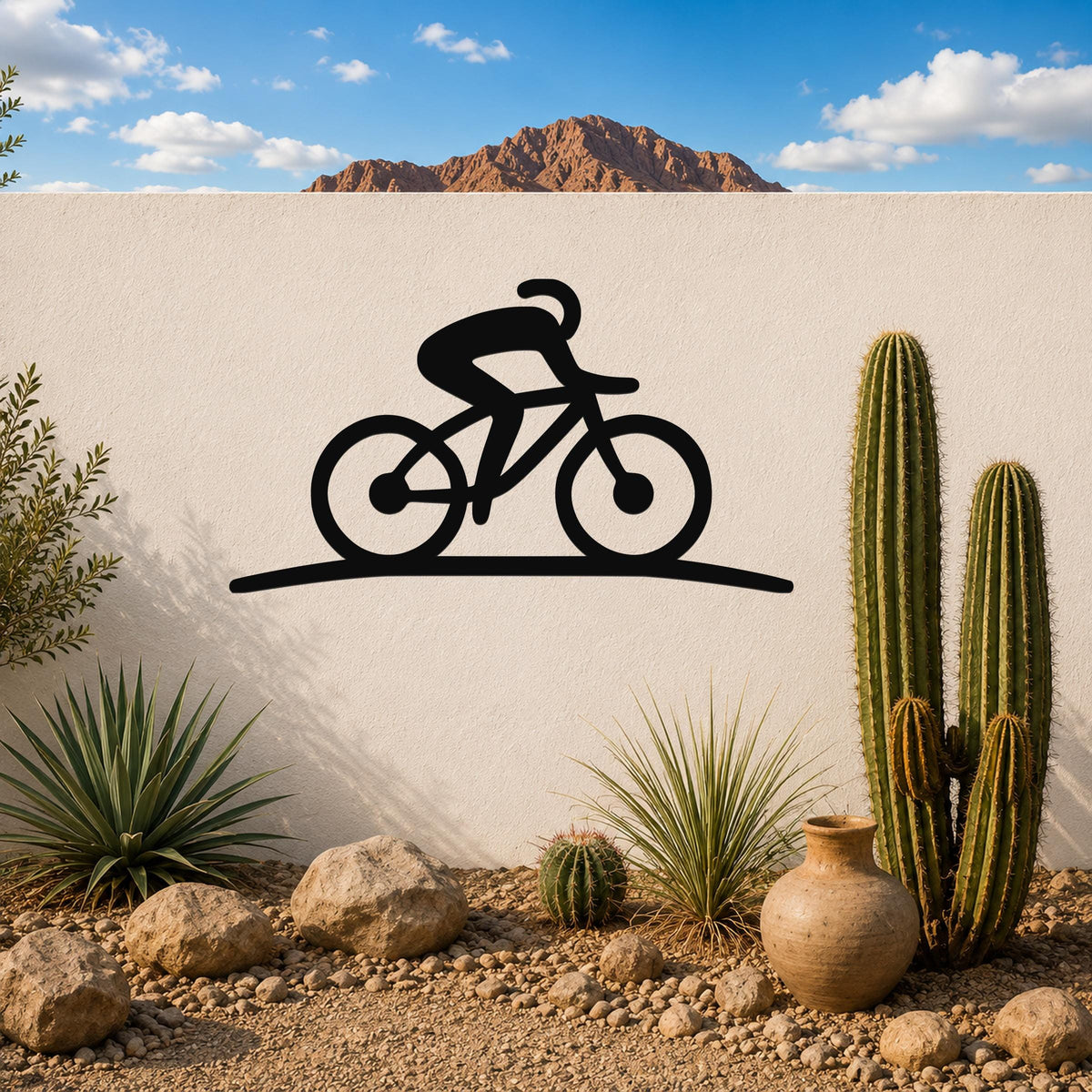 Black metal cycling wall art silhouette of a rider on a bike, mounted on a white outdoor wall above a desert garden with cacti and rocks.