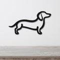 Black metal dachshund wall art in a silhouette cutout style, mounted on a white wall above a light wood surface.