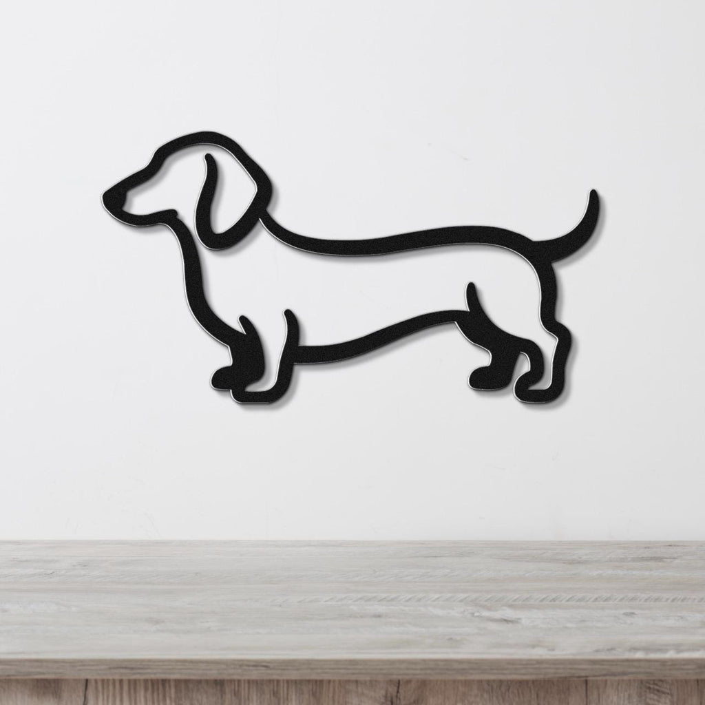 Black metal dachshund wall sculpture with a silhouette cutout design, mounted on a white wall above a light wood surface.