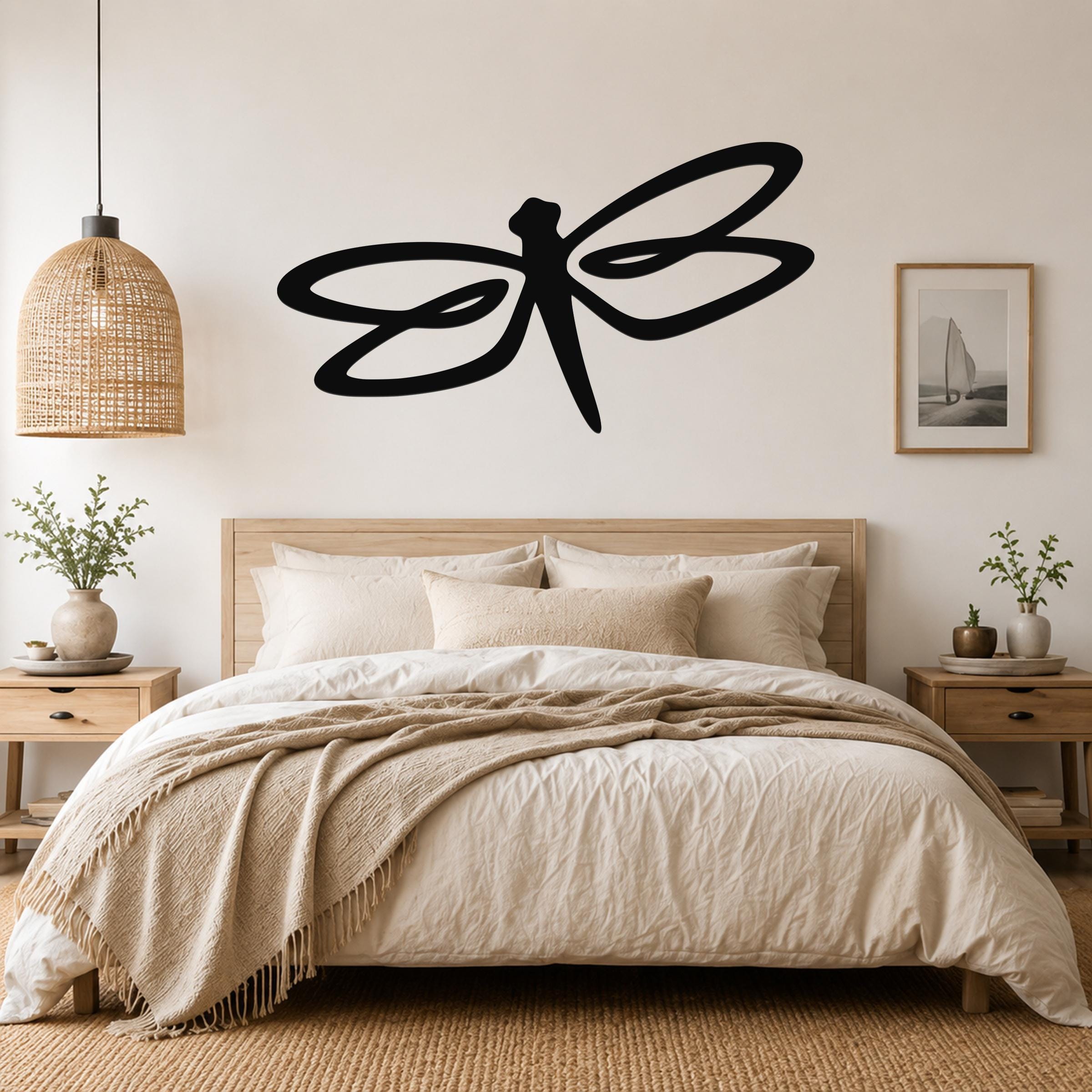 Black metal dragonfly wall art with flowing wing cutouts, mounted above a wooden bed in a neutral bedroom.