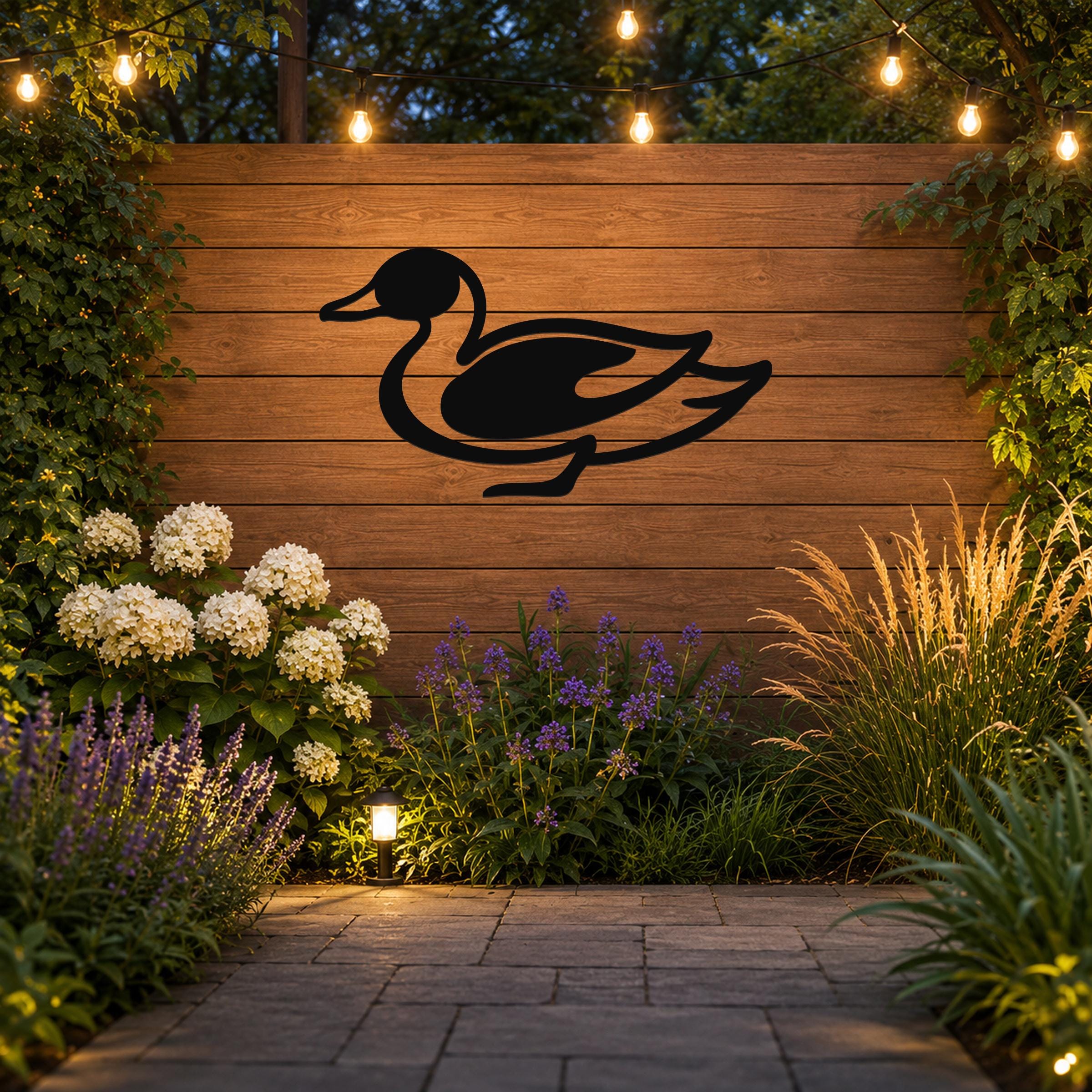 Black metal duck wall sculpture with a silhouette cutout, mounted on a wooden fence in an outdoor garden setting with string lights and plants.