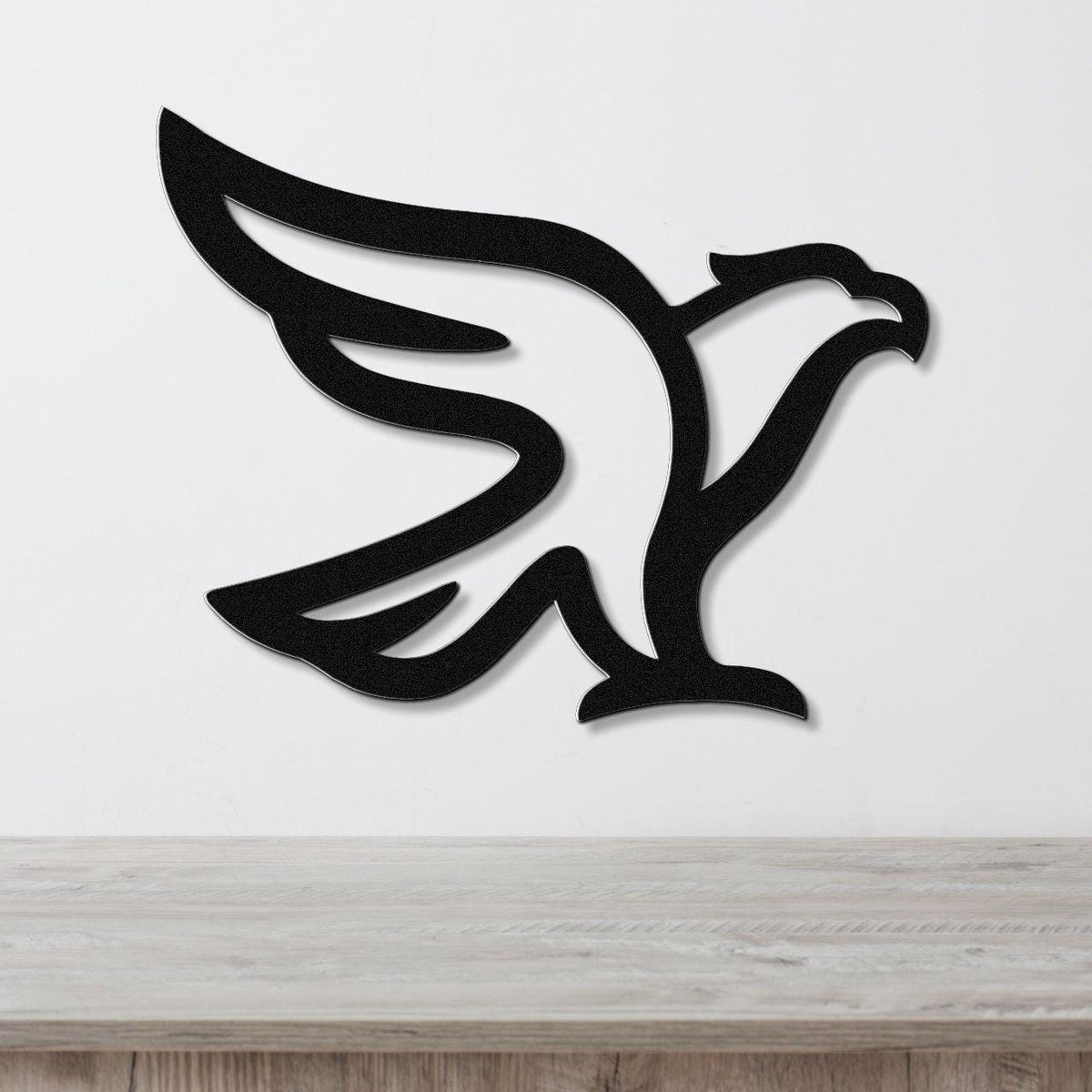 Black metal eagle wall art with a bold silhouette design, mounted on a white wall above a light wood surface.