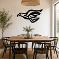 Black metal eagle wall art with flowing wing cutouts, mounted on a white wall above a wooden dining table in a bright dining room.