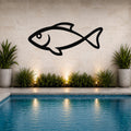 Black metal fish wall art silhouette mounted on a tiled outdoor wall above a pool, flanked by potted plants and illuminated by ground lights.