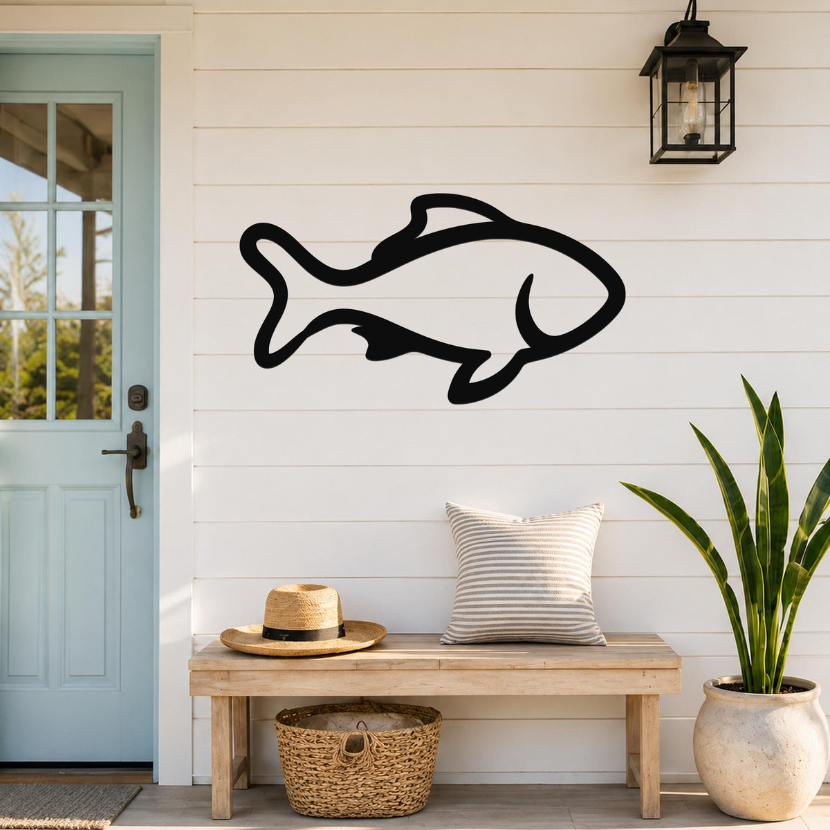 Black metal fish wall art with bold outline cutout, mounted on a white shiplap wall above a wooden bench in a coastal entryway.