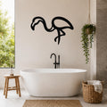 Black metal flamingo wall art silhouette mounted on a bathroom wall above a freestanding tub, with a hanging plant and woven basket nearby.