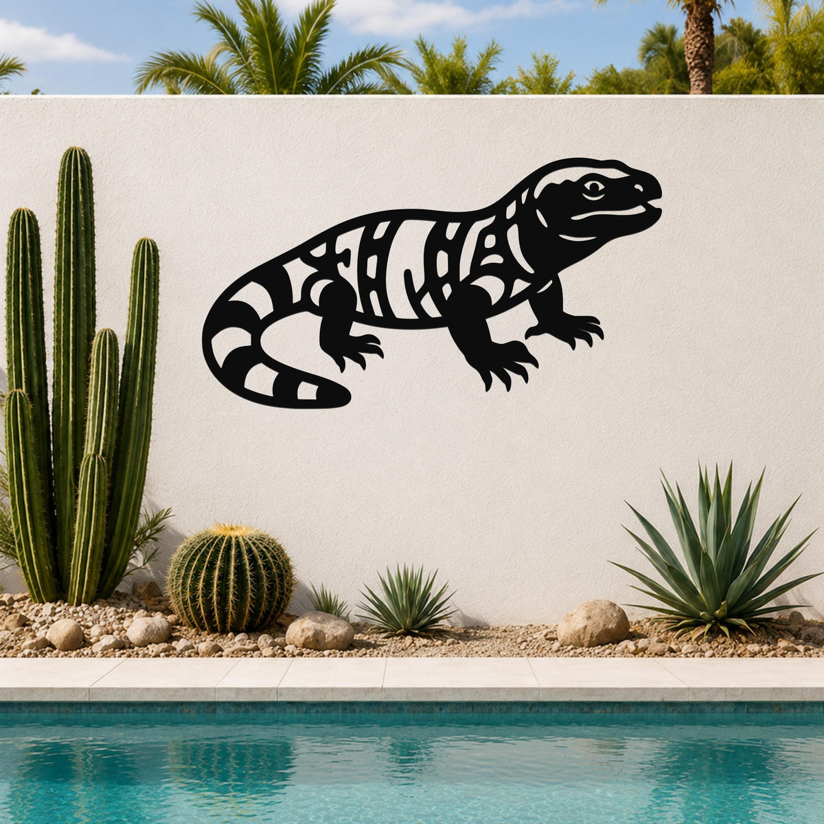 Black metal wall art of a Gila monster with intricate internal cutouts, mounted on a white outdoor wall above a pool with cacti and desert plants.