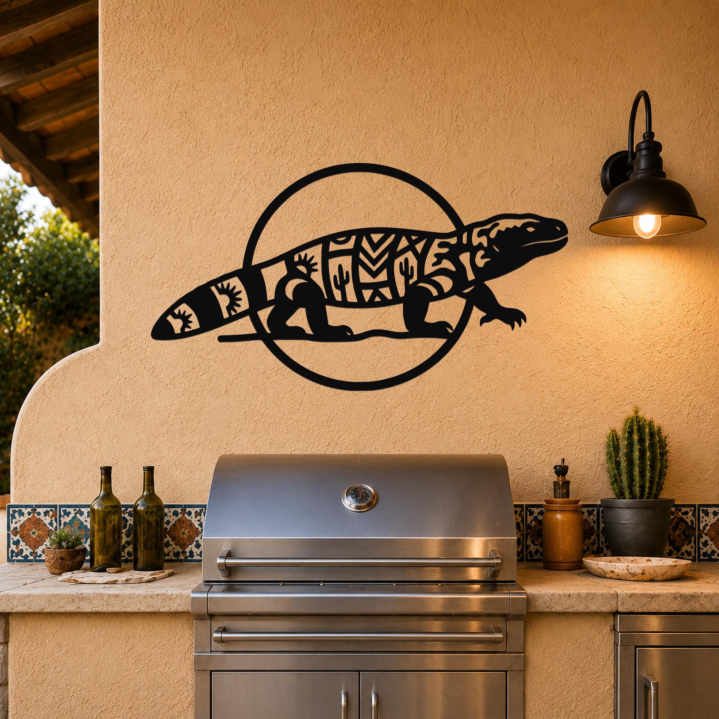 Black metal Gila monster wall art with geometric and cactus cutouts, mounted on a stucco wall above a stainless steel grill on an outdoor patio.