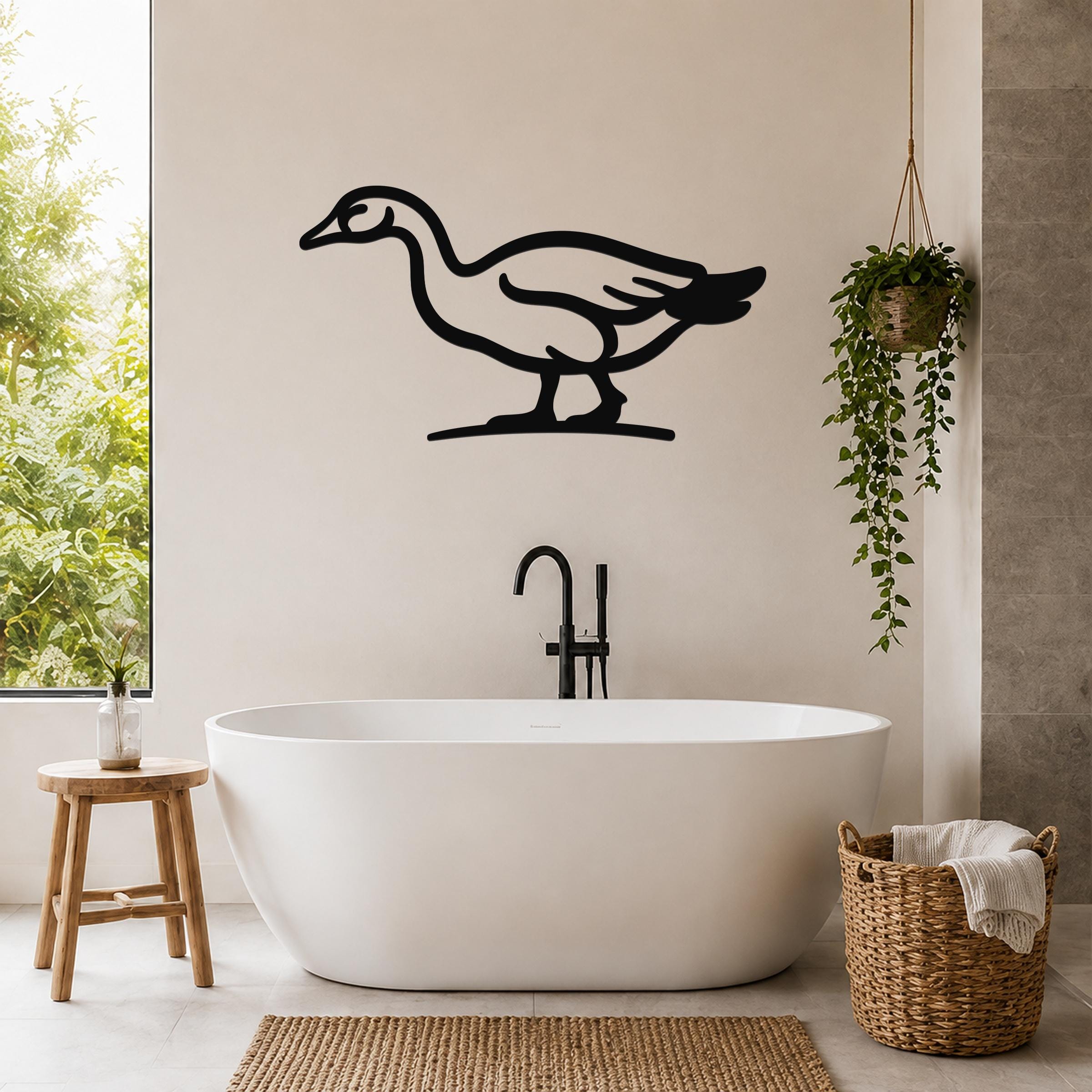 Black metal goose wall art silhouette mounted on a bathroom wall above a freestanding tub, with a hanging plant and woven basket nearby.