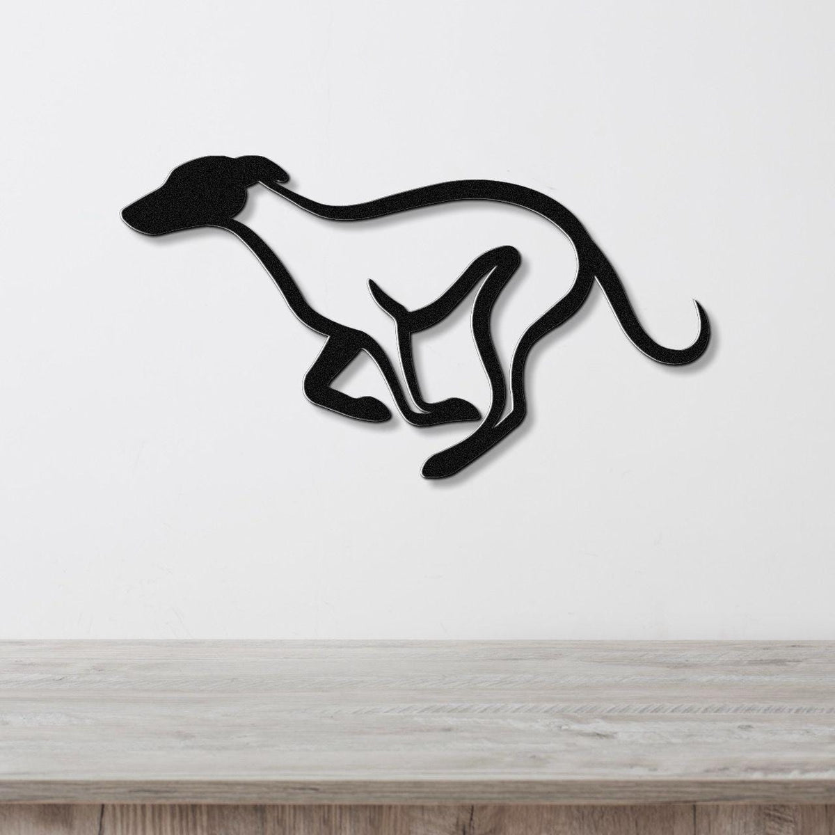Black metal greyhound wall art with a sleek silhouette and internal cutout legs, mounted on a white wall above a light wood counter.