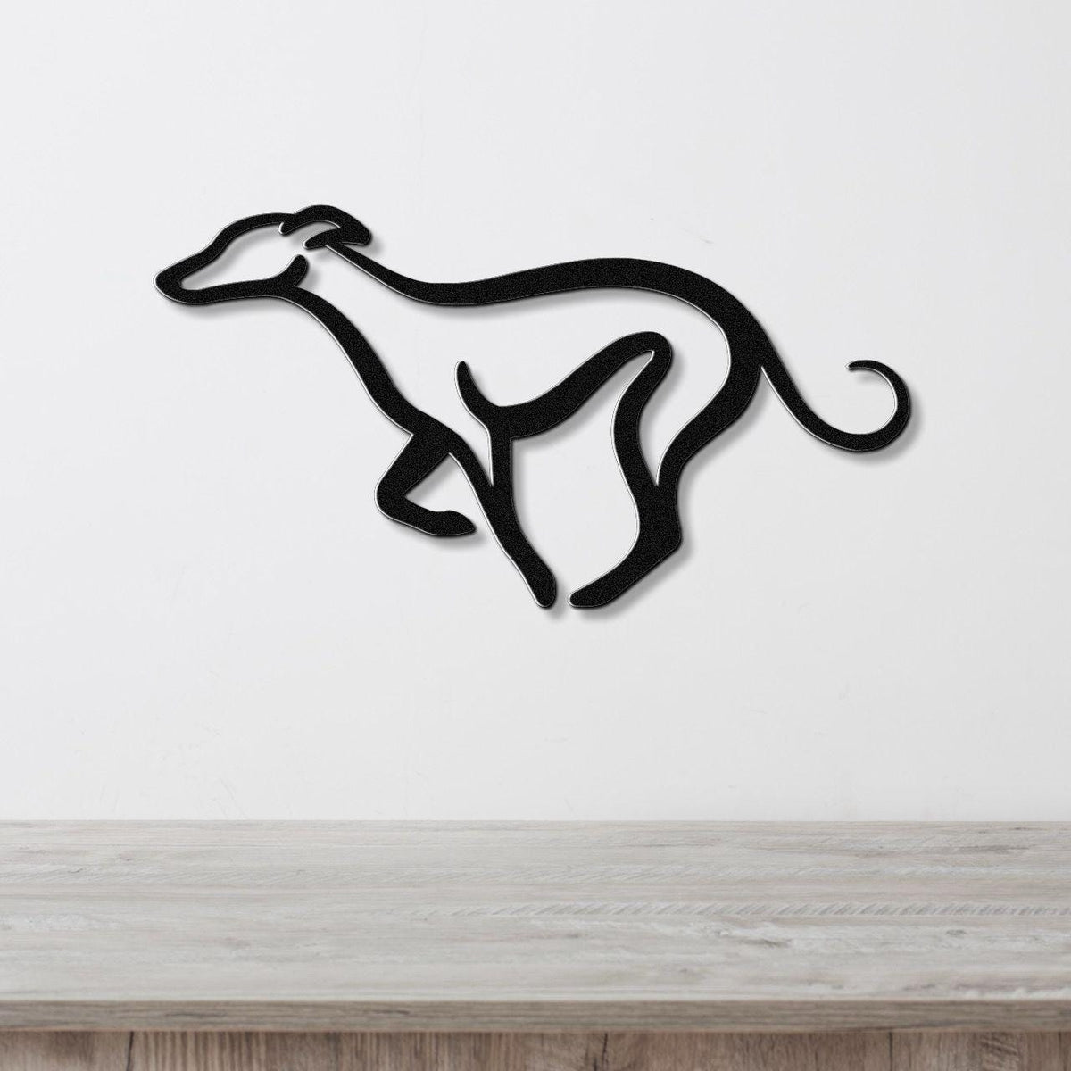 Black metal greyhound wall art with a minimalist silhouette design, mounted on a white wall above a light wood surface.