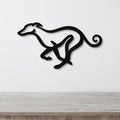 Black metal greyhound wall art with a sleek silhouette and curled tail, mounted on a white wall above a light wood surface.