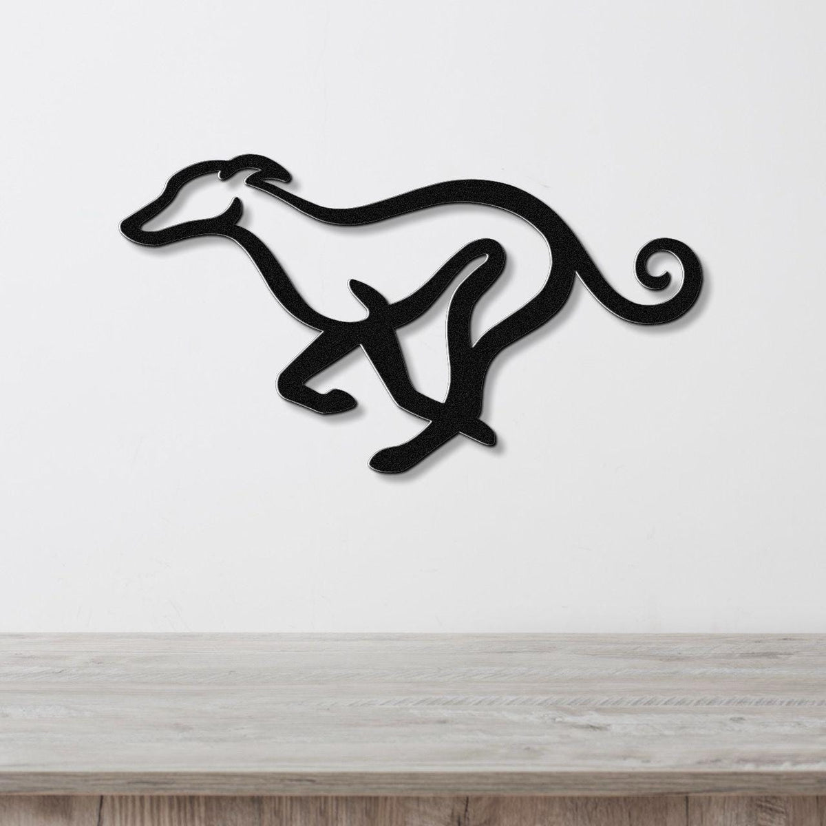 Black metal greyhound wall art with a sleek silhouette and curled tail, mounted on a white wall above a light wood surface.