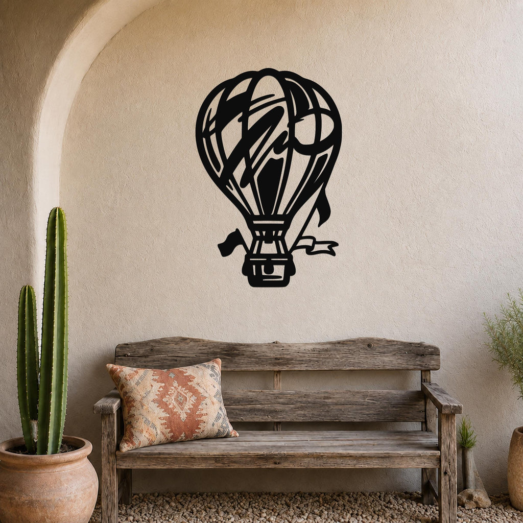 Black metal hot air balloon wall art with internal cutout details, mounted on a textured beige wall above a rustic wooden bench in a patio setting.