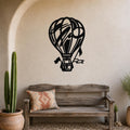 Black metal hot air balloon wall art with internal cutout details, mounted on a textured beige wall above a rustic wooden bench in a patio setting.