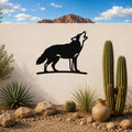 Black metal coyote wall art in a howling silhouette, mounted on a white outdoor wall above a desert garden with cacti and rocks.