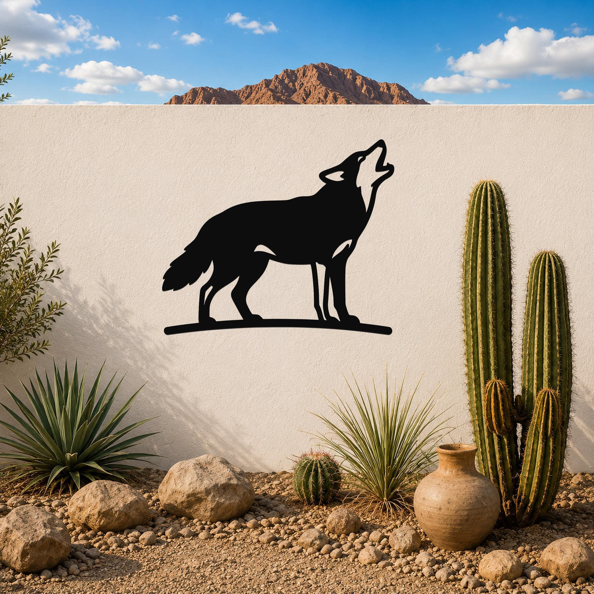 Black metal coyote wall art in a howling silhouette, mounted on a white outdoor wall above a desert garden with cacti and rocks.