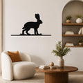 Black metal jackrabbit wall art silhouette mounted on a living room wall above a white armchair, with a wooden coffee table and built-in shelves visible nearby.