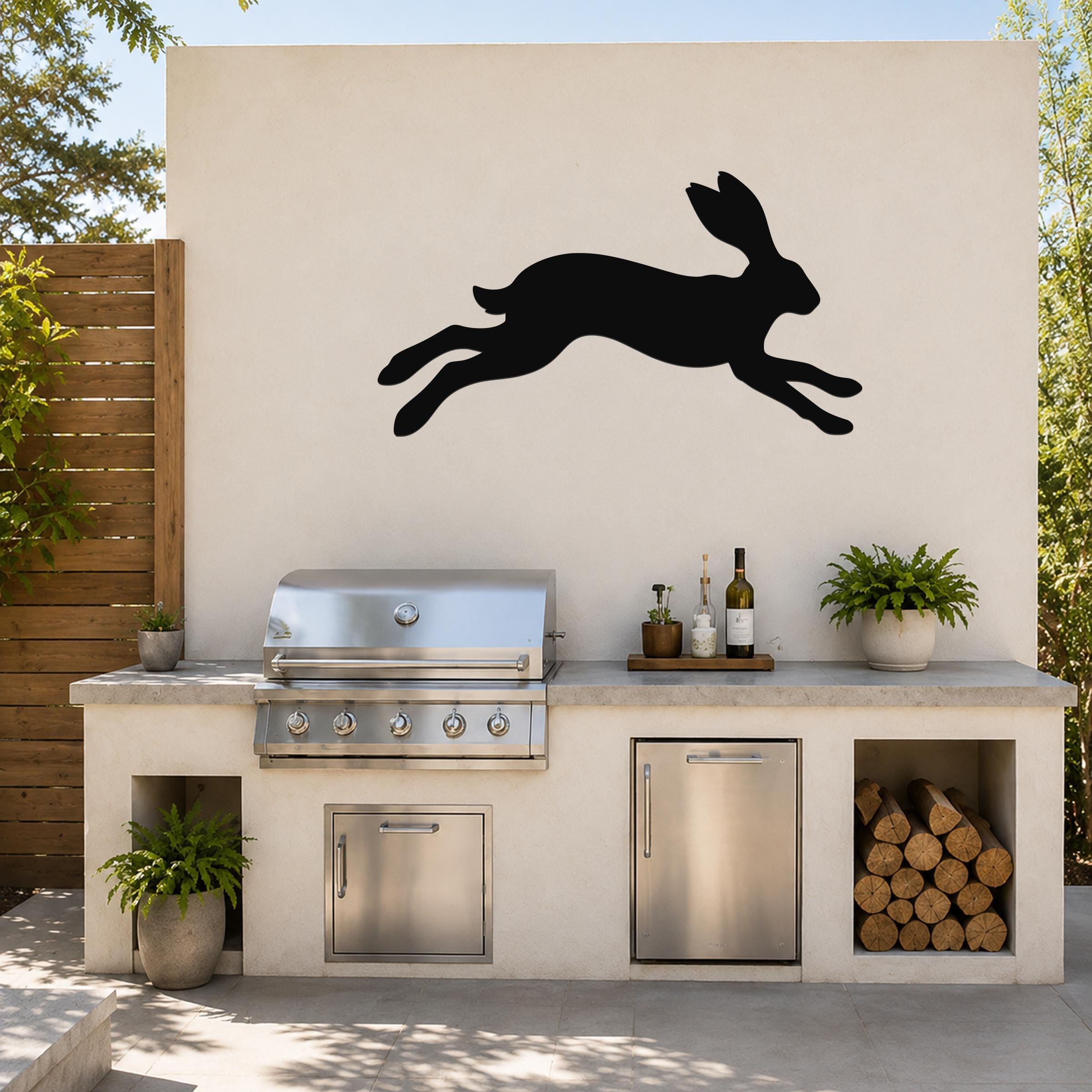 Black metal jackrabbit wall art silhouette mounted on a light-colored outdoor wall above a kitchen counter with a grill and plants.