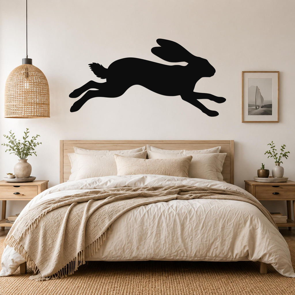 Black metal jackrabbit wall art silhouette with motion lines, mounted above a bed in a neutral bedroom.