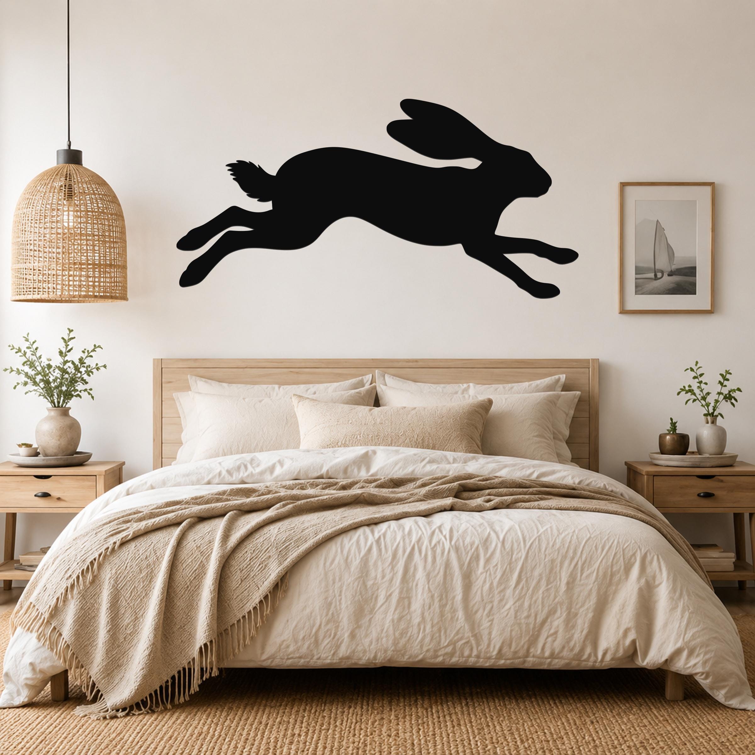 Black metal jackrabbit wall art silhouette with motion lines, mounted above a bed in a neutral bedroom.