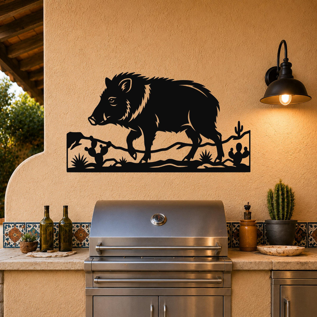 Black metal wall art featuring a javelina silhouette with cacti and desert plants, mounted on an outdoor wall above a stainless steel grill.