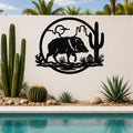 Black metal wall art featuring a javelina silhouette with cactus and desert landscape cutouts, mounted on a white outdoor wall beside a pool.