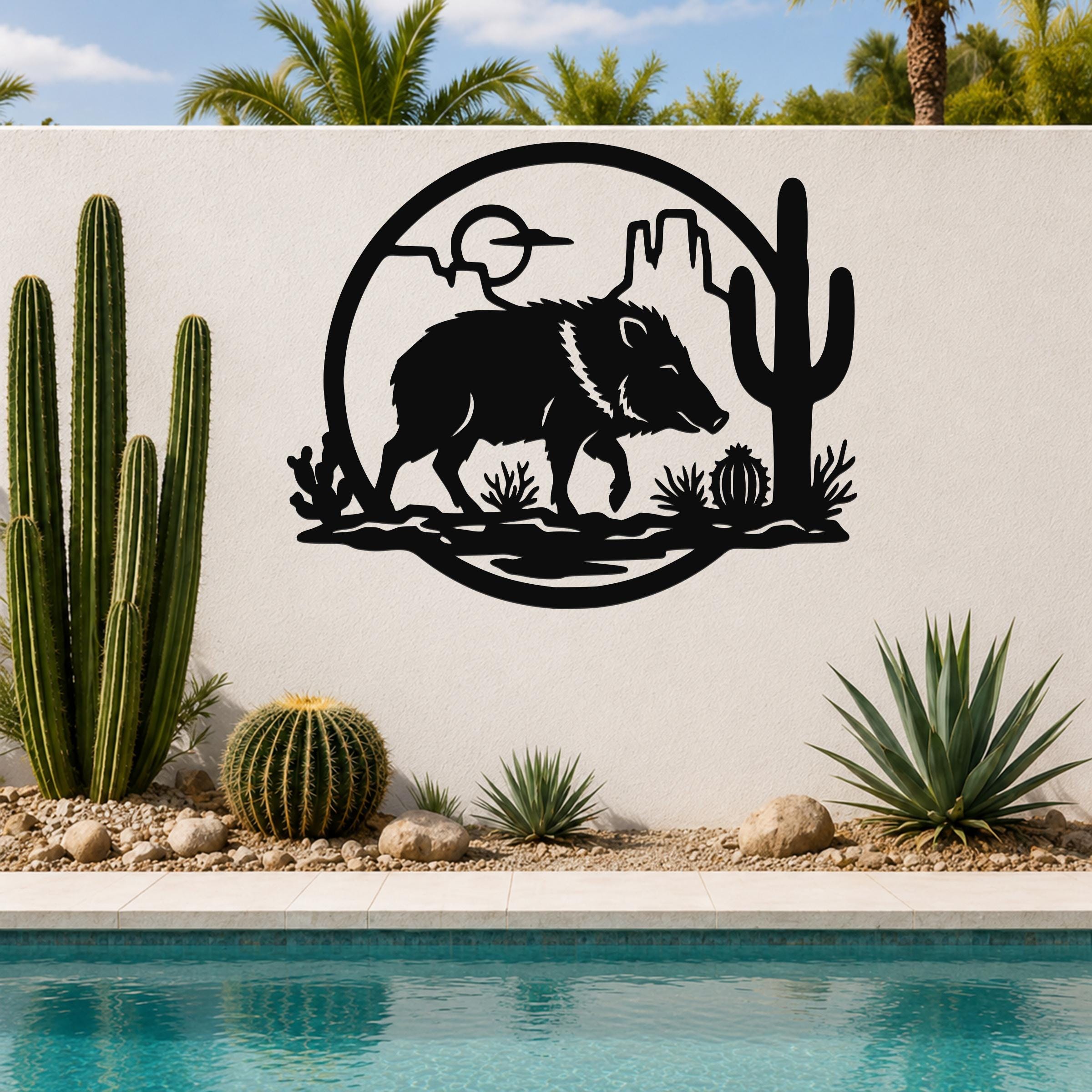 Black metal wall art featuring a javelina silhouette with cactus and desert landscape cutouts, mounted on a white outdoor wall beside a pool.